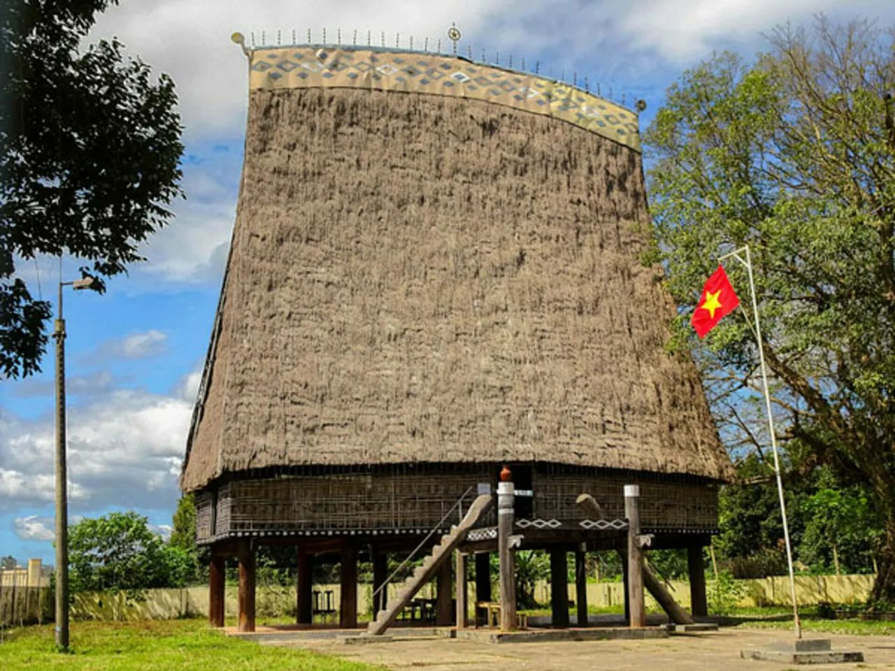 The tall thatched roof of the Kon Klor rong house standing on wooden stilts beside trees