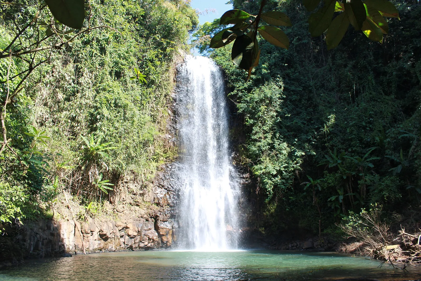 Pa Sy Waterfall dropping into a green pool surrounded by forest in Mang Den
