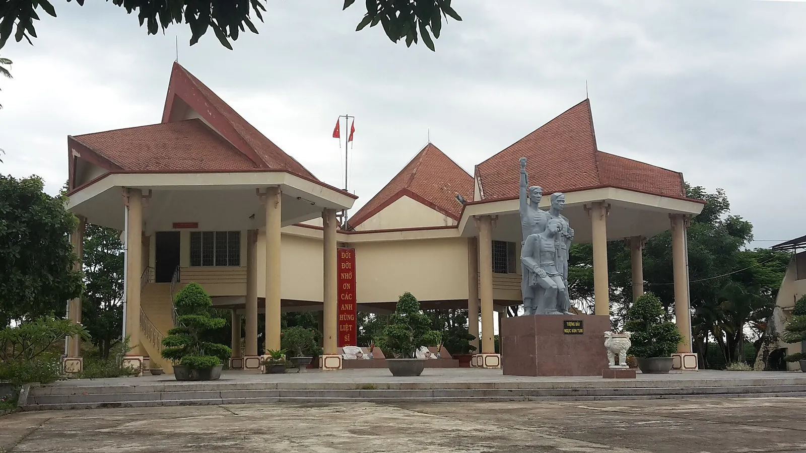 The Kon Tum Prison memorial site, with a statue in front of a building with red tiled roofs