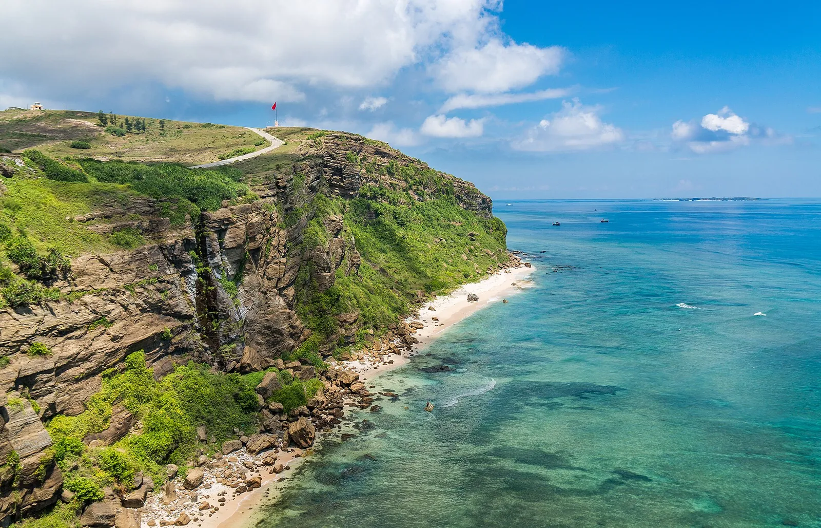 Green volcanic headland dropping to a narrow white beach and turquoise sea on Ly Son Island