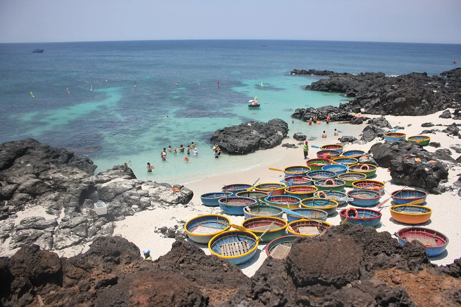 Round basket boats lined up on a white-sand beach between black volcanic rocks on the Small Island of Ly Son