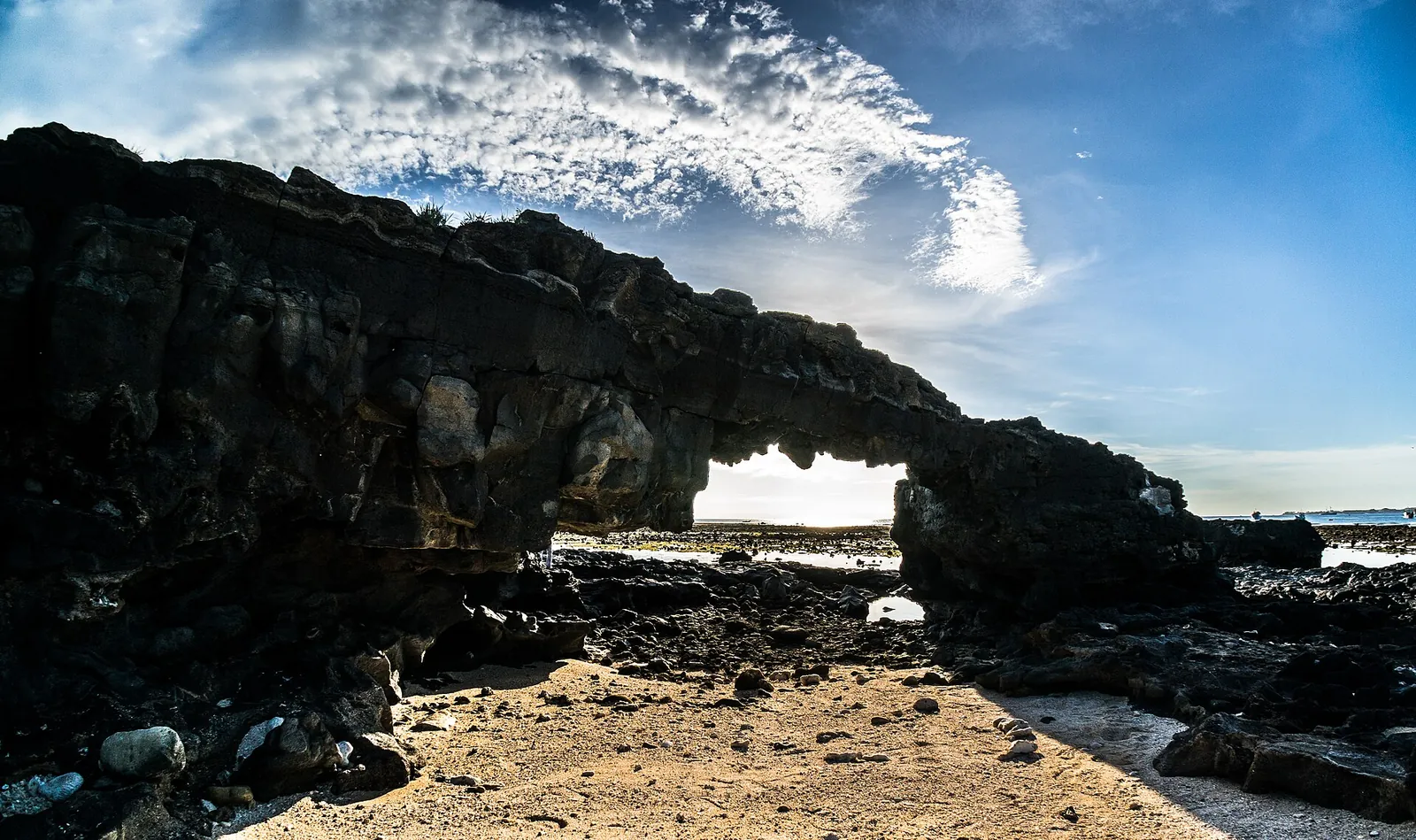 Natural arch of black basalt rock on a sandy shore of Ly Son under a blue sky