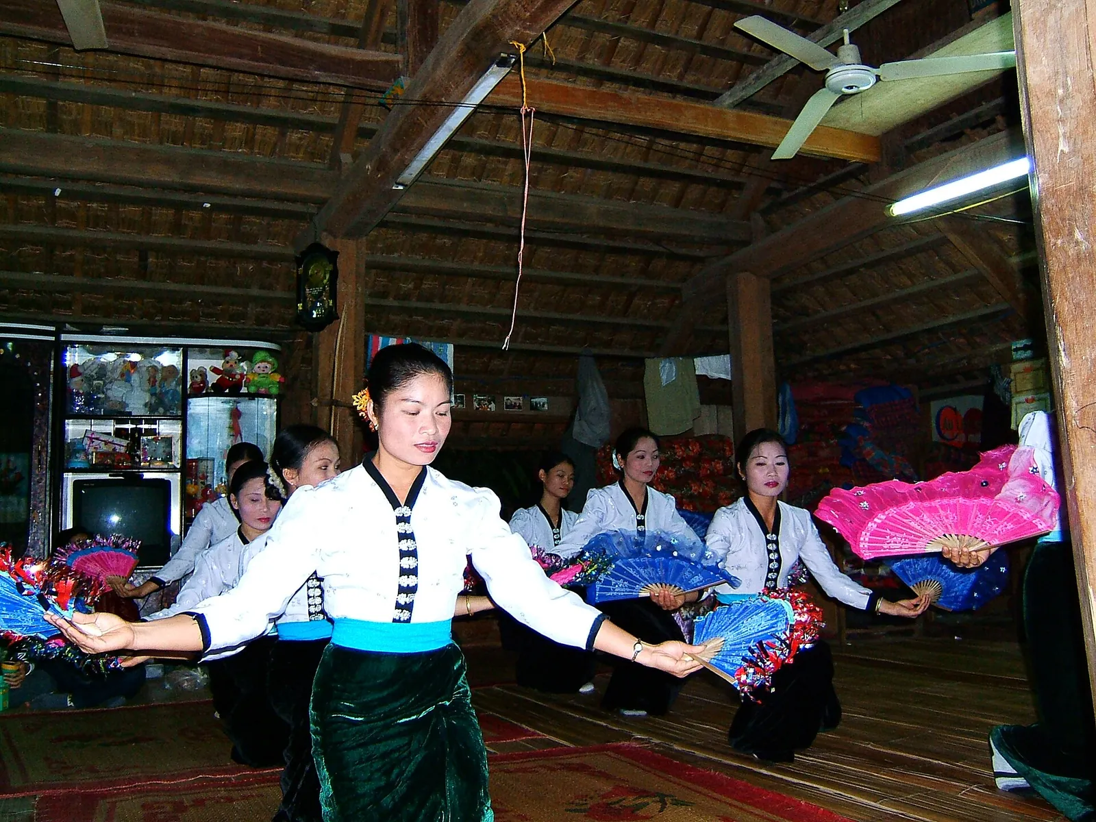 White Thai women in white blouses and long skirts performing a fan dance inside a wooden stilt house at Ban Lac
