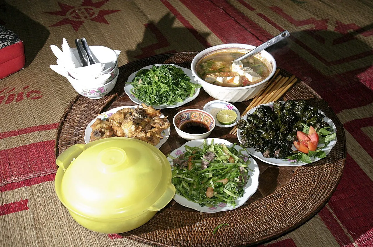 A shared meal on a woven tray in Mai Chau: soup, stir-fried greens, fried dishes, dipping sauces and a lidded rice pot
