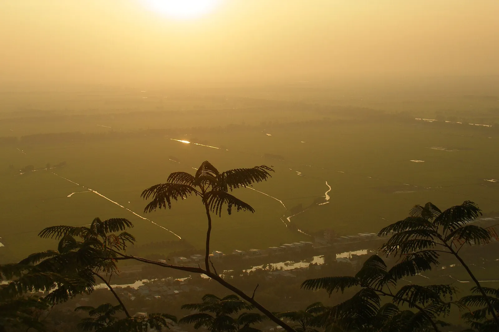 Hazy evening sun over the flat rice plains seen from the slopes of Sam Mountain, Chau Doc