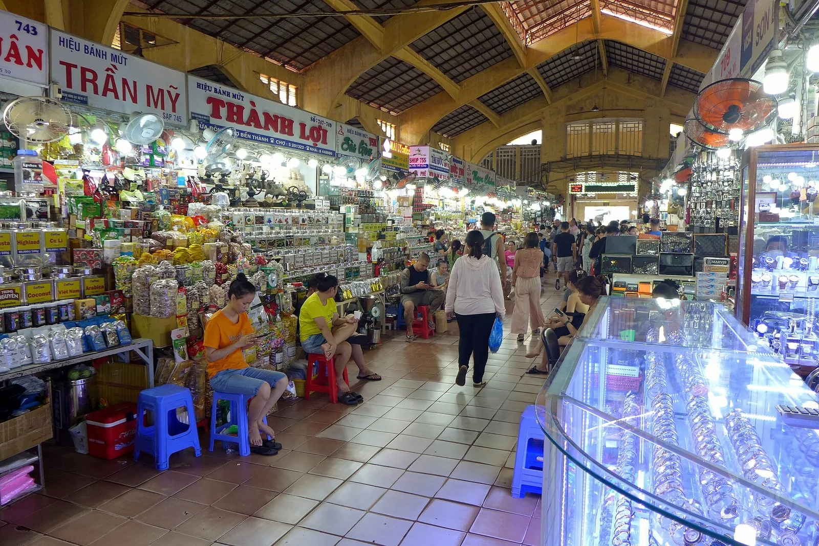 Busy aisle of sweet and snack stalls under the high roof of Ben Thanh Market in Ho Chi Minh City