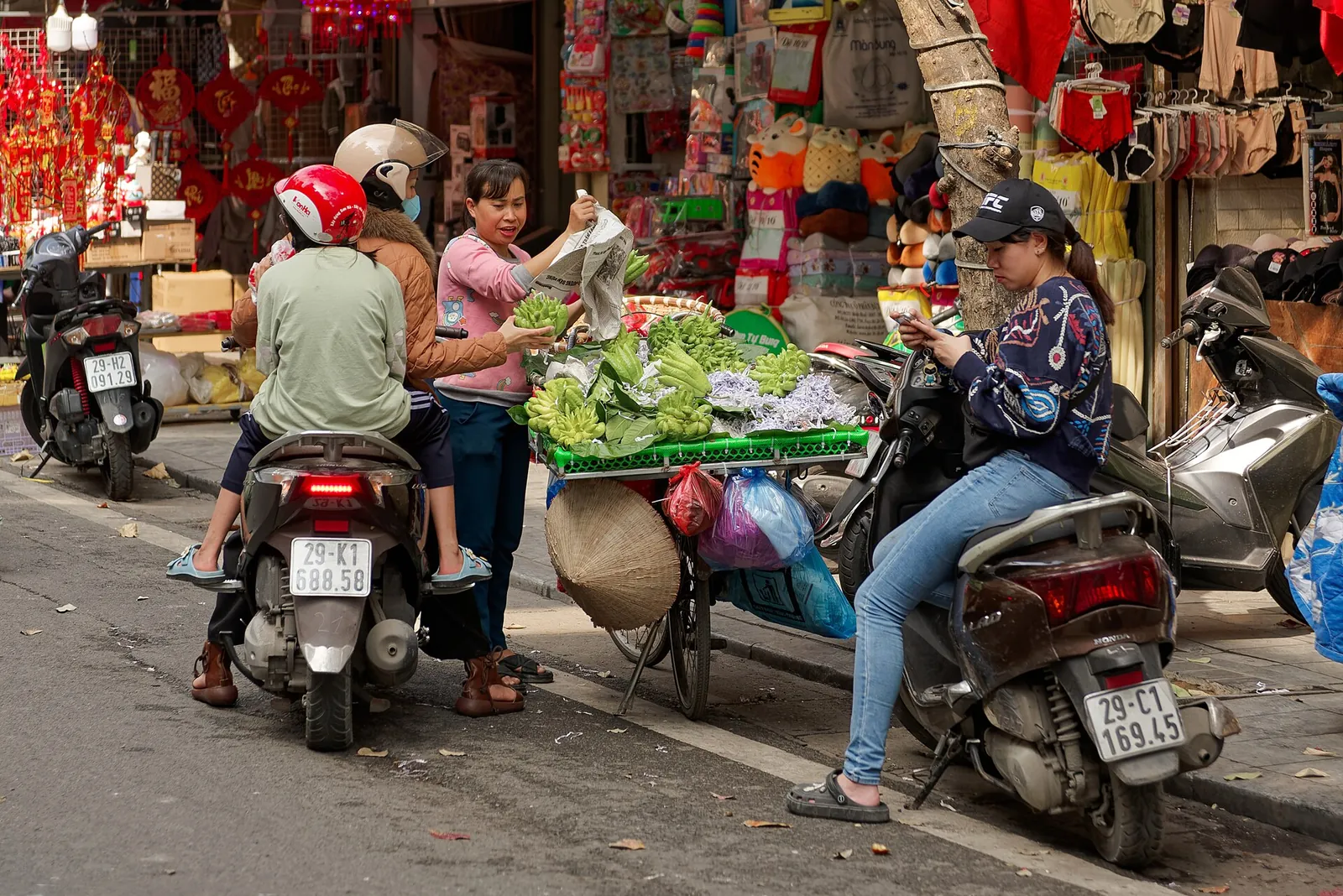 A street seller sells fingered citrons and greens from a bicycle to a couple on a motorbike in Hanoi's Old Quarter