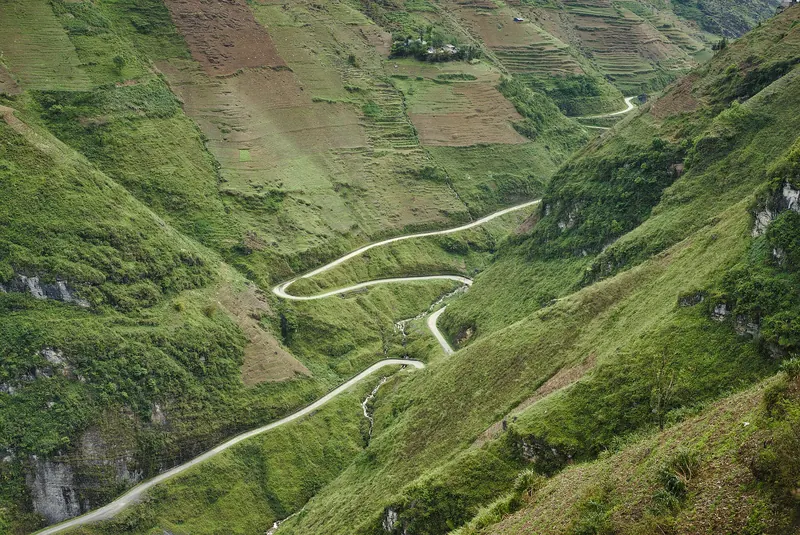 A narrow road winding in loops down a green mountainside at the Ma Pi Leng Pass, Ha Giang