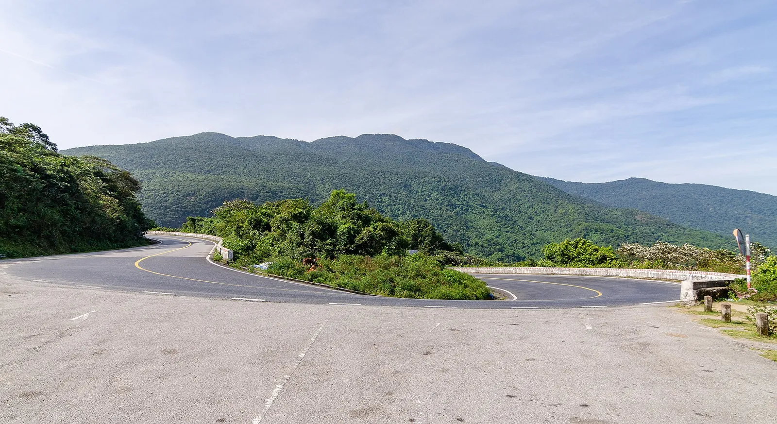A hairpin bend on the Hai Van Pass road with forested hills behind under a blue sky