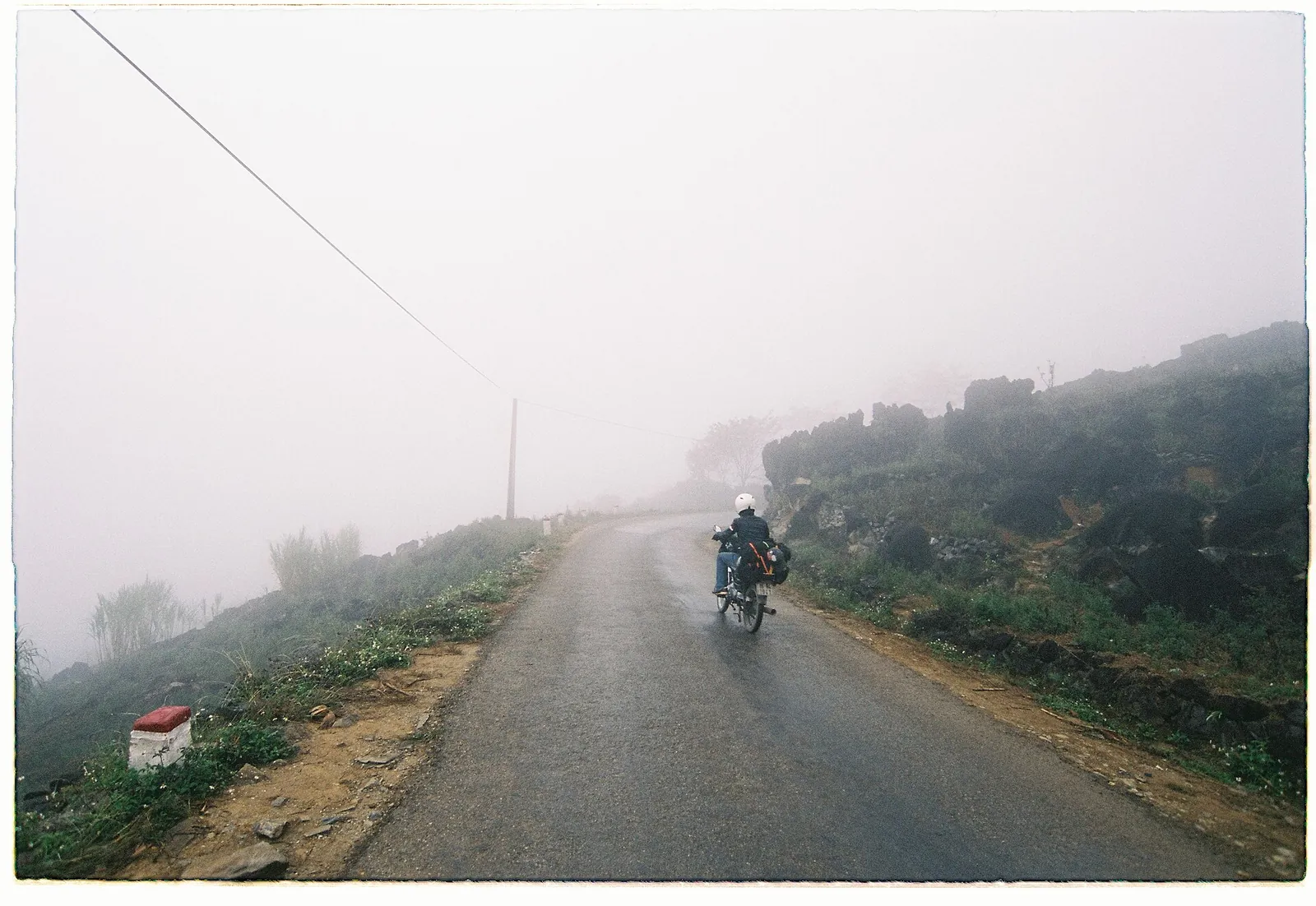A lone motorbike rider on a wet mountain road in thick fog in Ha Giang