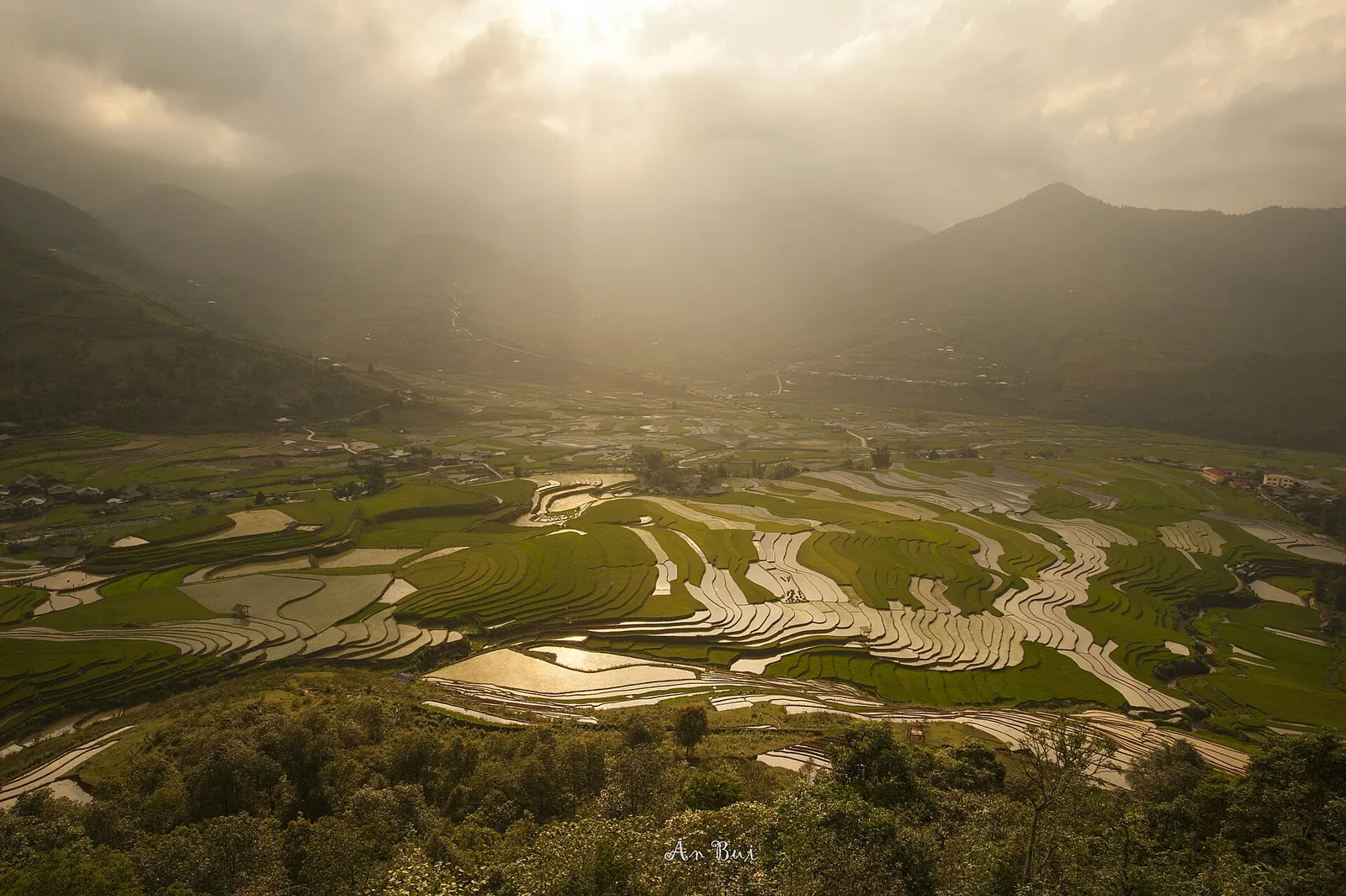 Tu Le valley with patches of flooded terraces under hazy sunlight and mountains