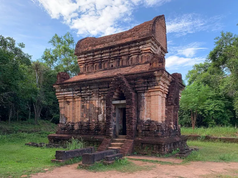 Brick Cham tower-temple E7 at My Son Sanctuary under a blue sky, surrounded by lawn and jungle