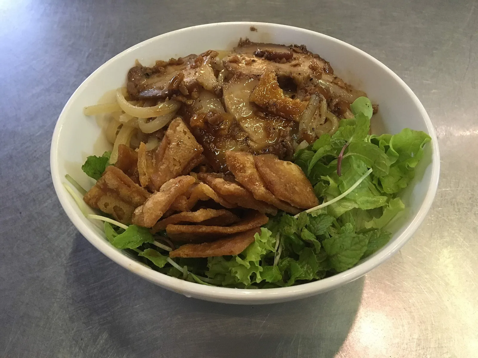 A bowl of cao lau noodles with pork slices, crisp crackers and green herbs