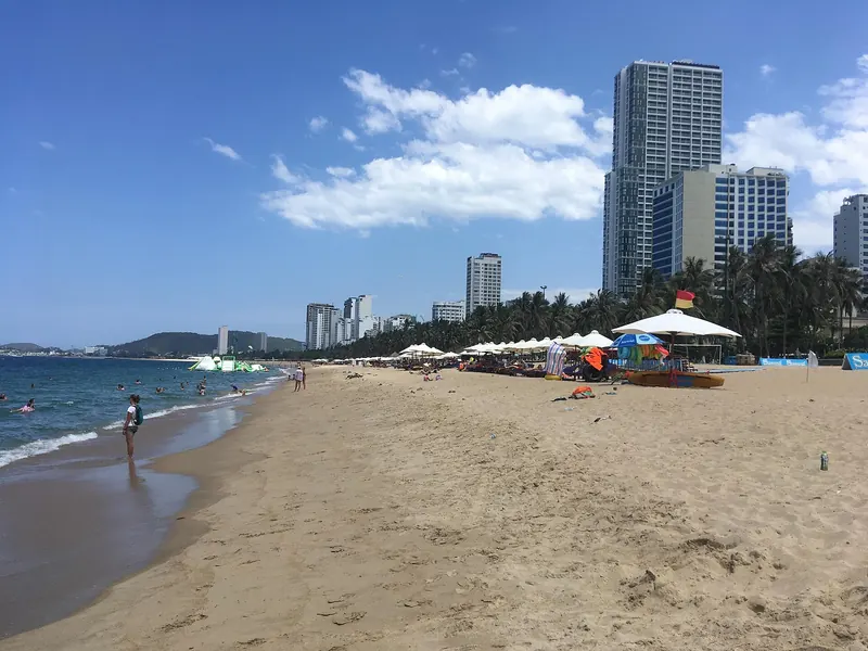 Nha Trang's main city beach with sun umbrellas, swimmers and high-rise hotels along the shore under a blue sky