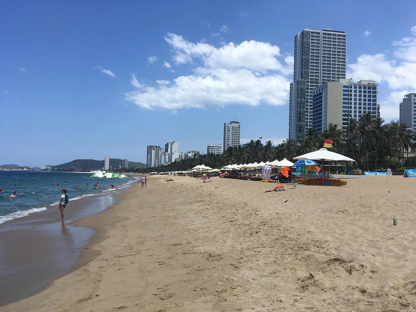 Nha Trang's main city beach with sun umbrellas, swimmers and high-rise hotels along the shore under a blue sky