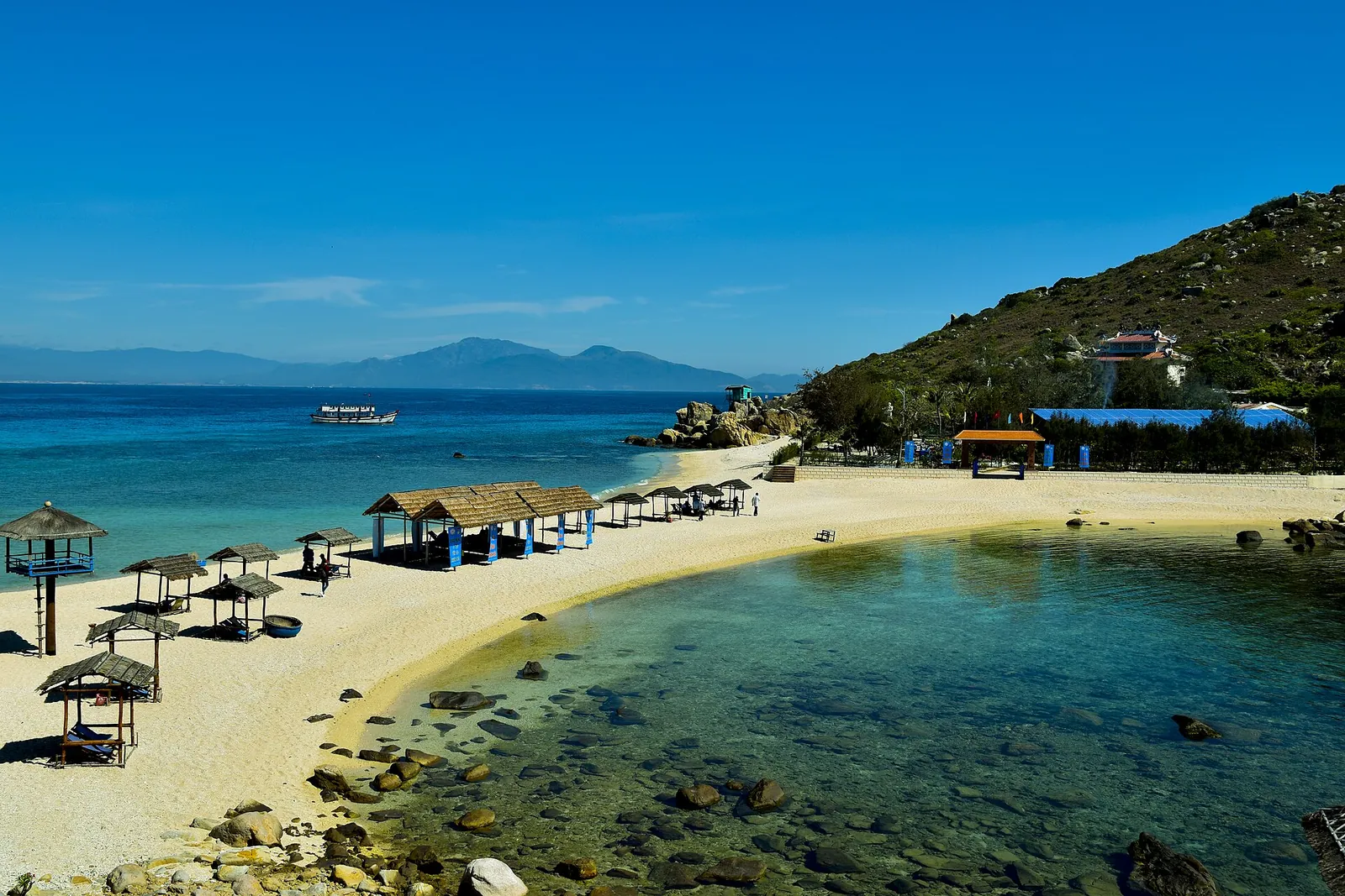 Small sandy beach with thatched umbrellas and clear turquoise water on Hon Noi island in Nha Trang Bay