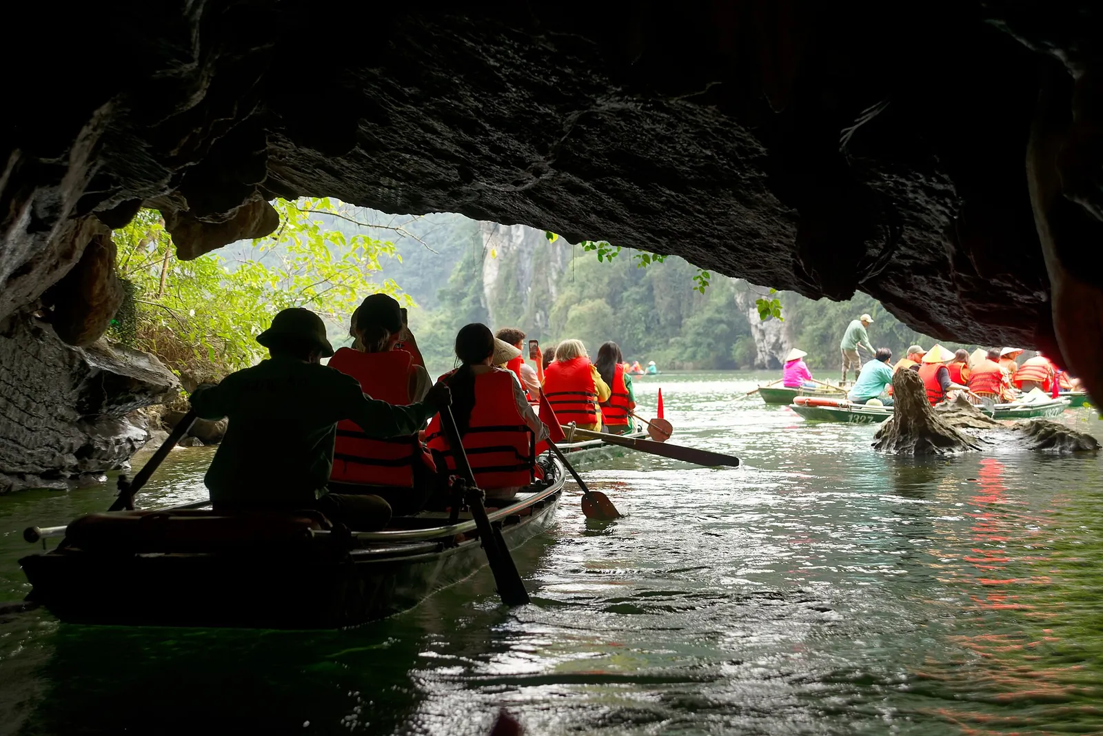 Rowing boats with passengers in life jackets passing through a low cave at Trang An