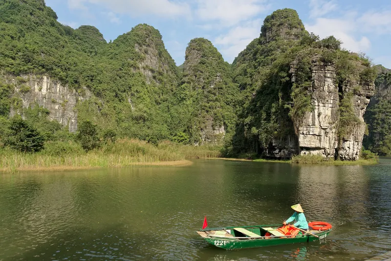 Limestone karst peaks above a green river with a rowing boat at Trang An, Ninh Binh