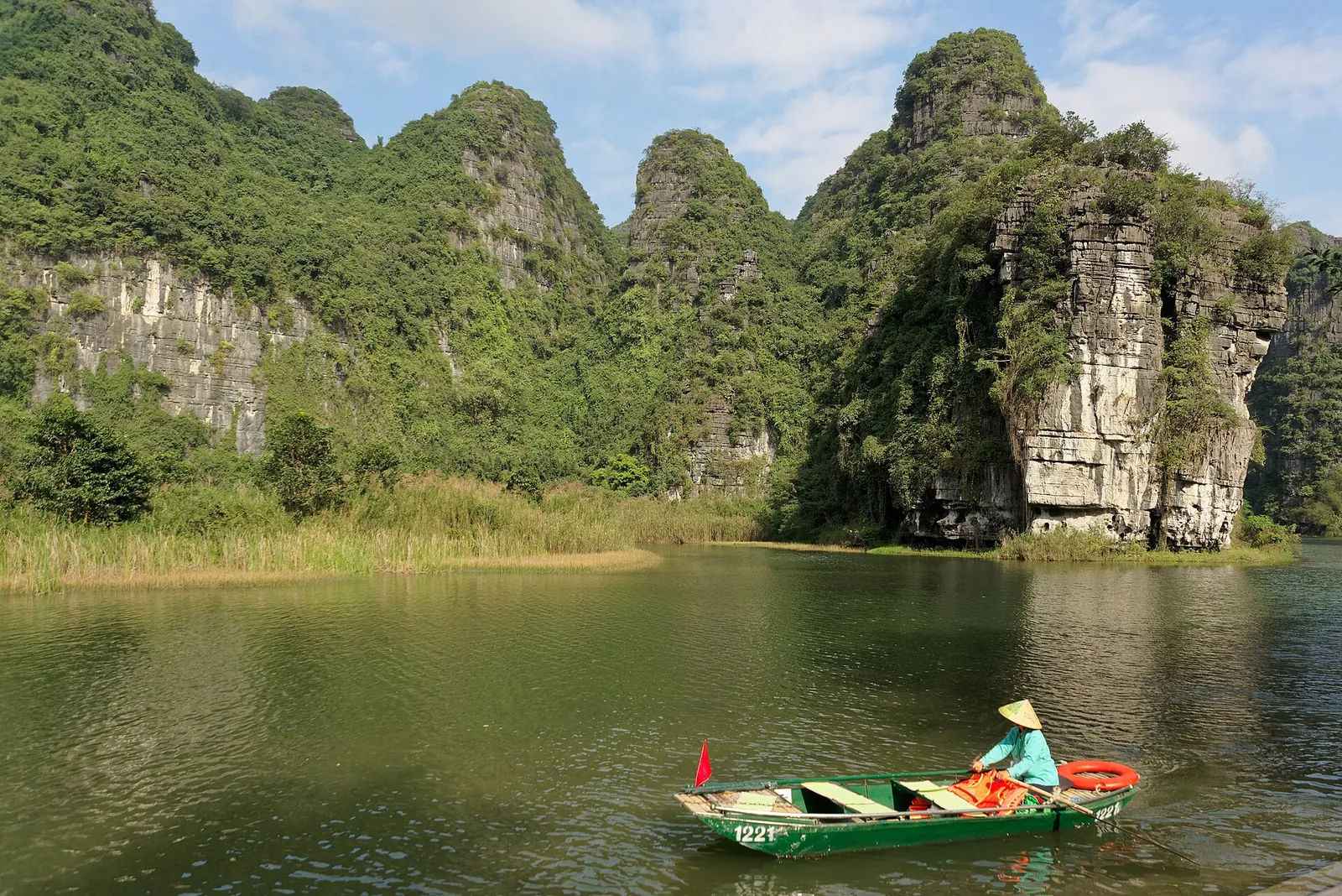 Limestone karst peaks above a green river with a rowing boat at Trang An, Ninh Binh