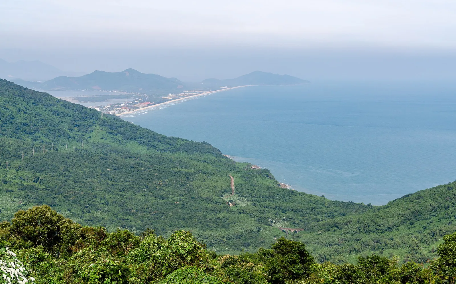 Forested slopes of the Hai Van Pass dropping to the sea, with the Lang Co shoreline in the distance