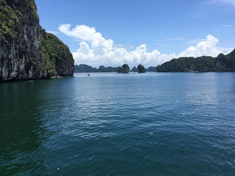 Limestone islands rising from blue water under a bright sky in Lan Ha Bay