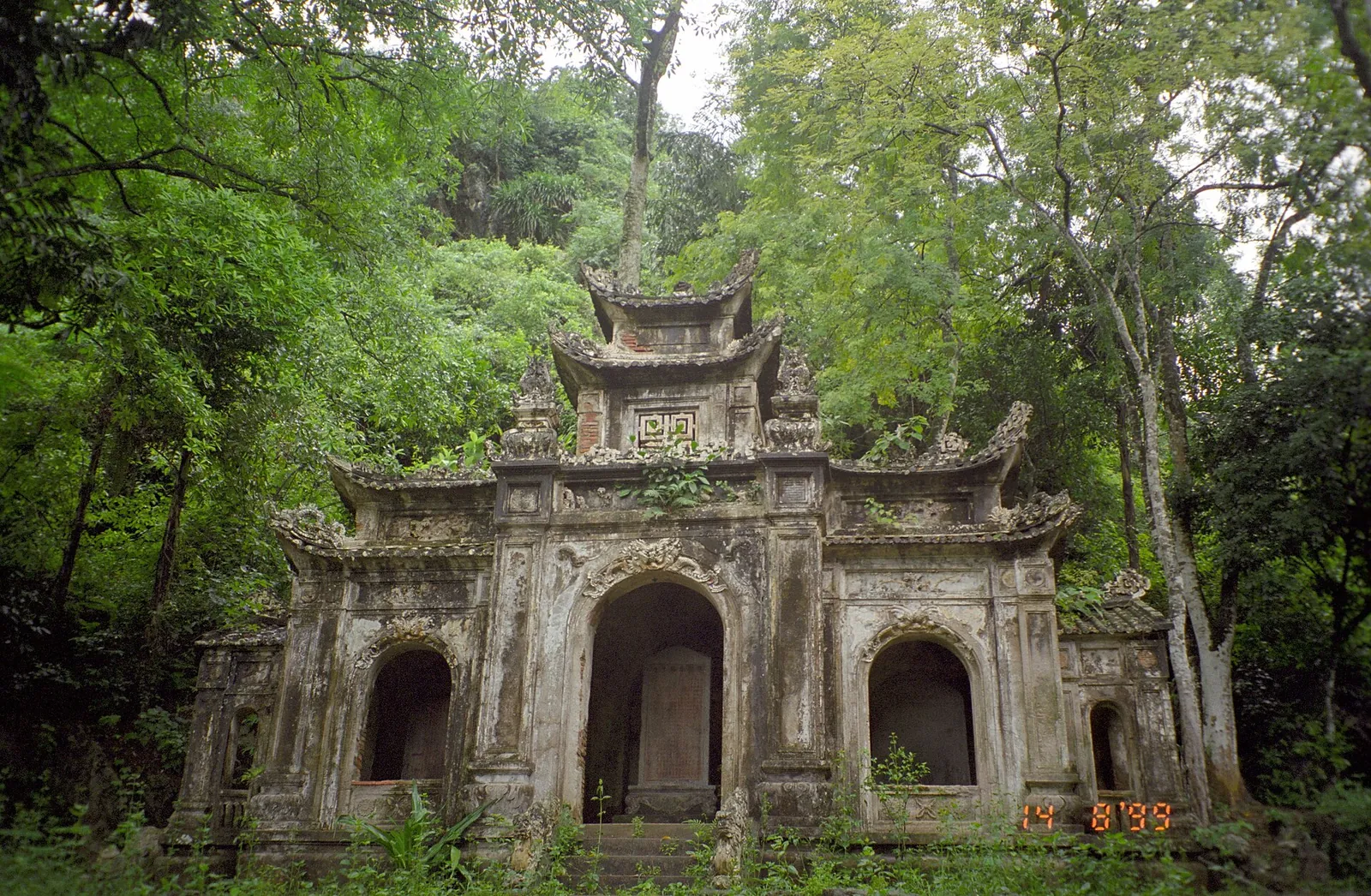 An old moss-covered stone gateway among trees in the Perfume Pagoda complex