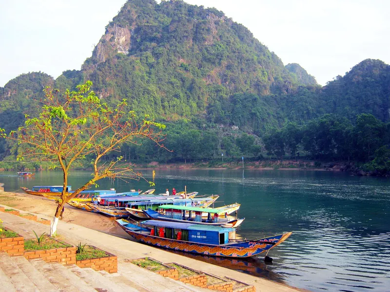 Tour boats moored along the Son River below forested limestone peaks at Phong Nha