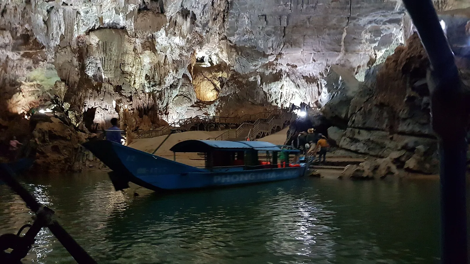 A wooden tour boat on the underground river inside Phong Nha Cave, with lit rock formations behind