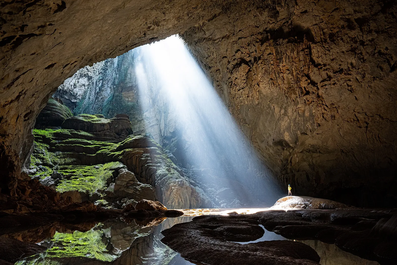 A beam of sunlight falling through a doline into Son Doong cave onto a small figure below