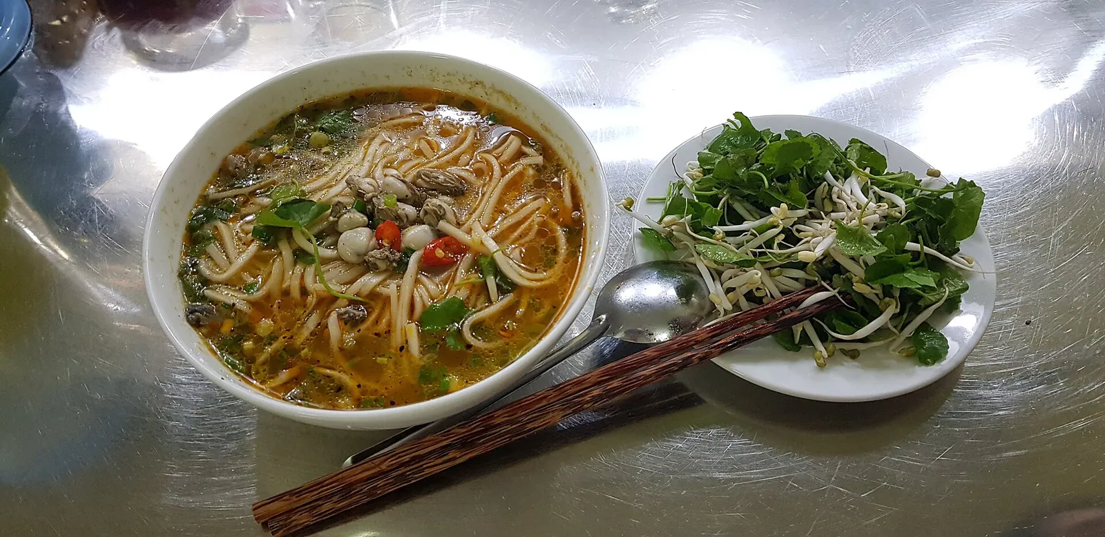 A bowl of chao canh noodle soup with oysters, herbs and chopsticks on a table in Dong Hoi