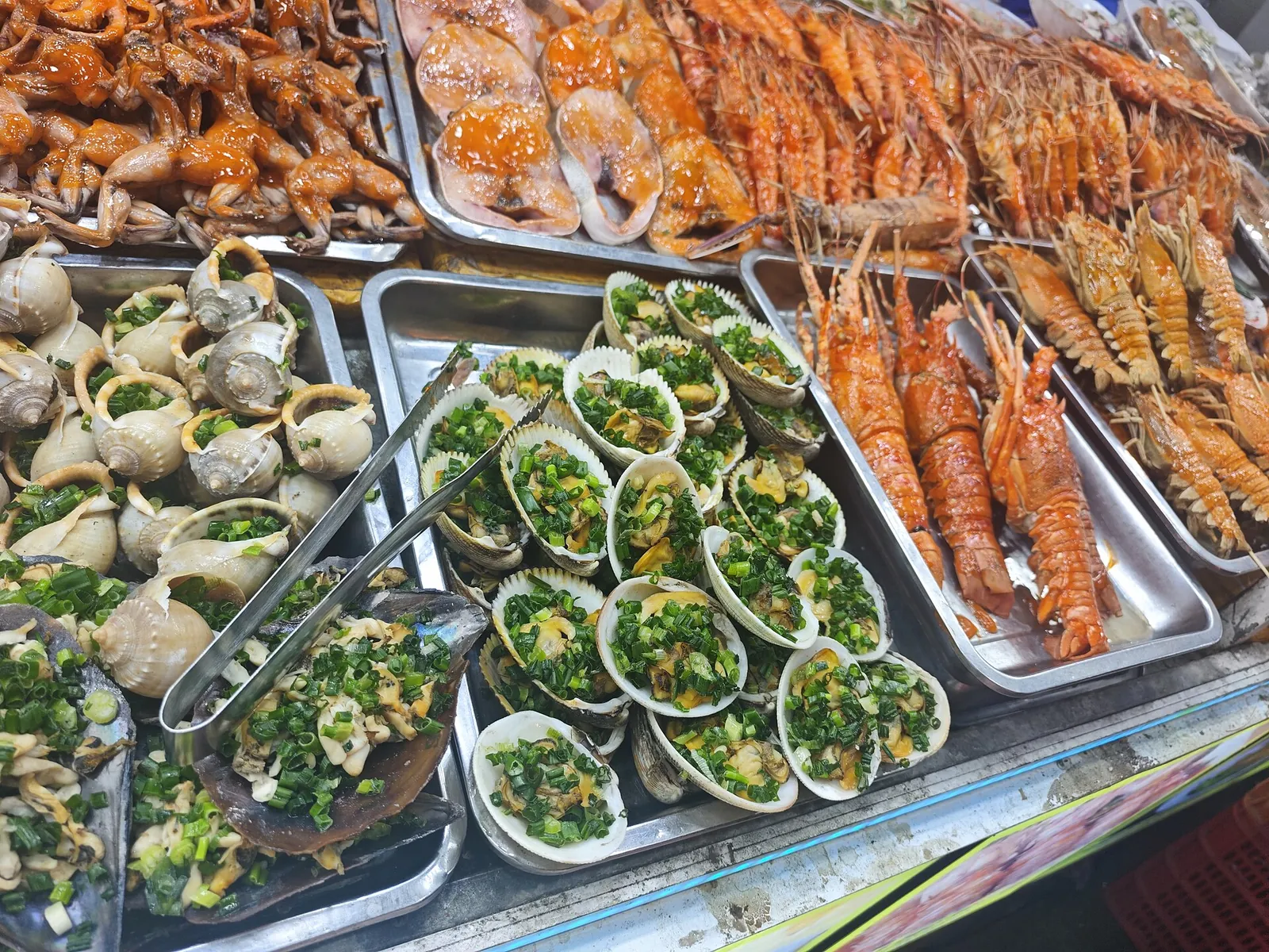 Trays of lobsters, mantis shrimp, sea snails and scallops topped with spring onion, laid out at a Phu Quoc night-market stall