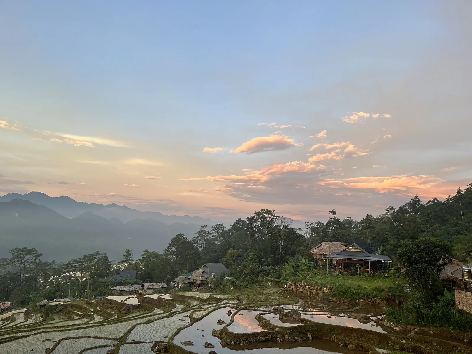 Sunset over flooded rice terraces and stilt houses in Pu Luong with mountains on the horizon