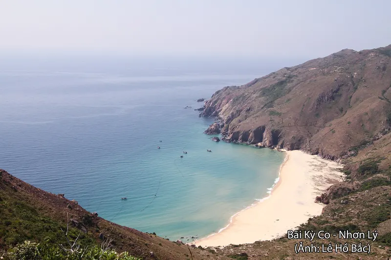 Ky Co beach, a white-sand cove below steep hills, with turquoise water and small boats in the bay