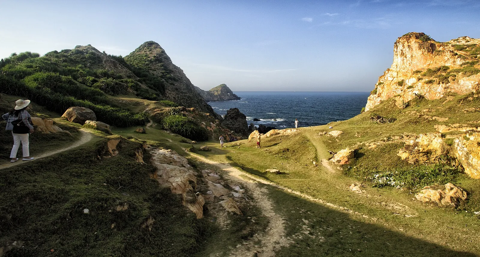 A walker on a path across grassy, wind-worn cliffs above the sea at Eo Gio