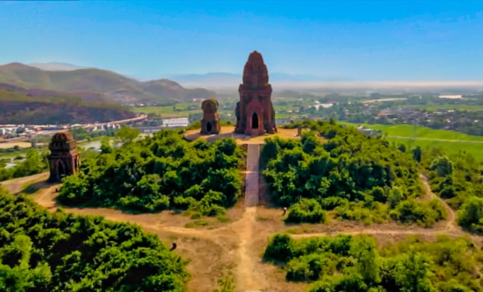 Brick Cham towers on a green hilltop above fields, a town and distant hills
