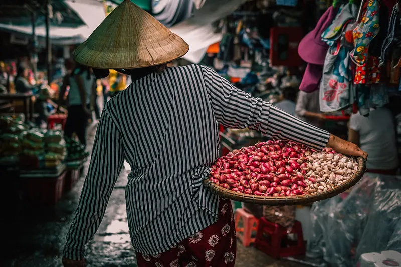 Vendor in a conical hat holding a tray of red beans among stalls at Dong Ba Market in Hue