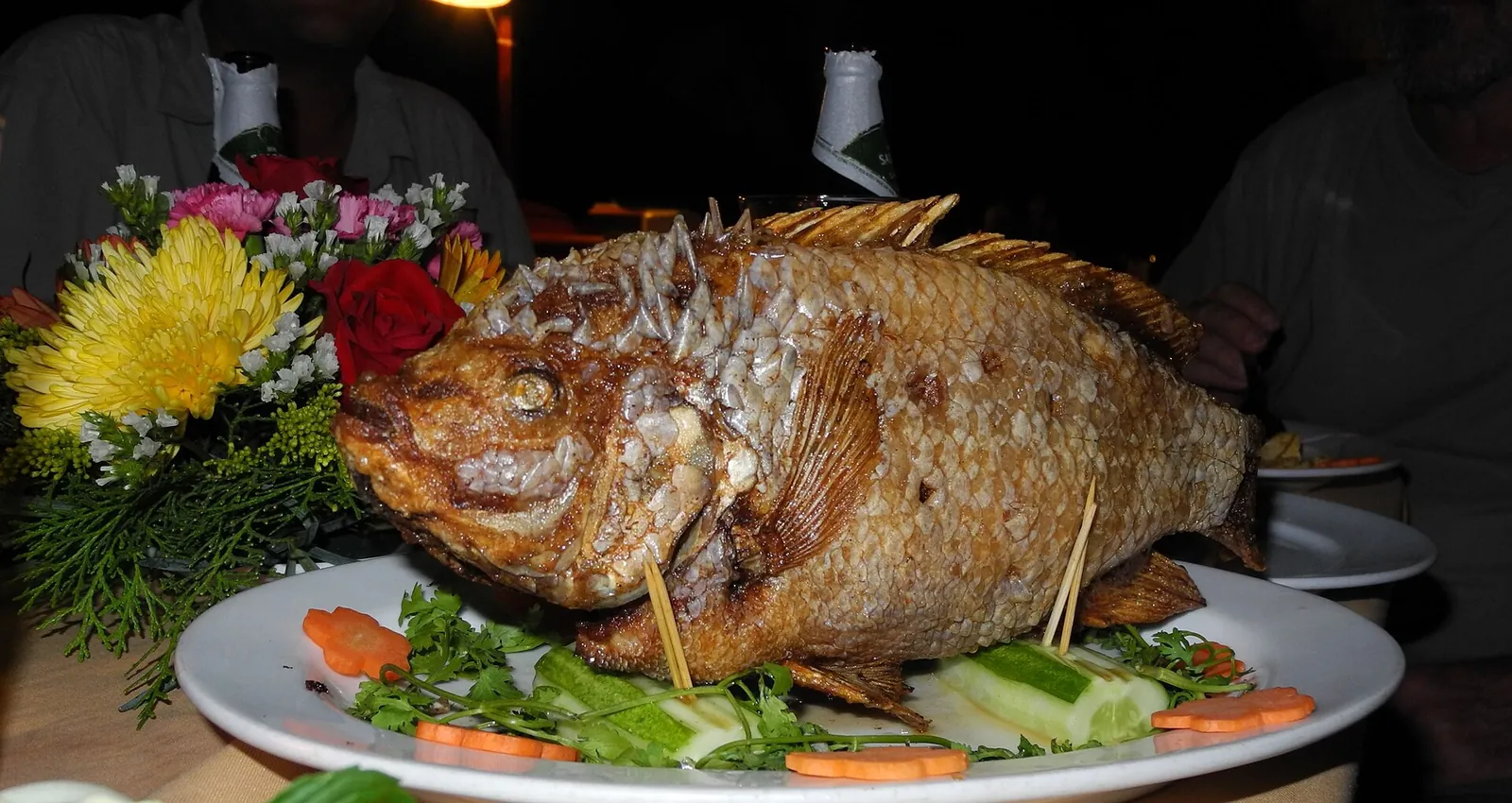 Whole fried elephant ear fish standing upright on a platter with herbs and flowers in Can Tho