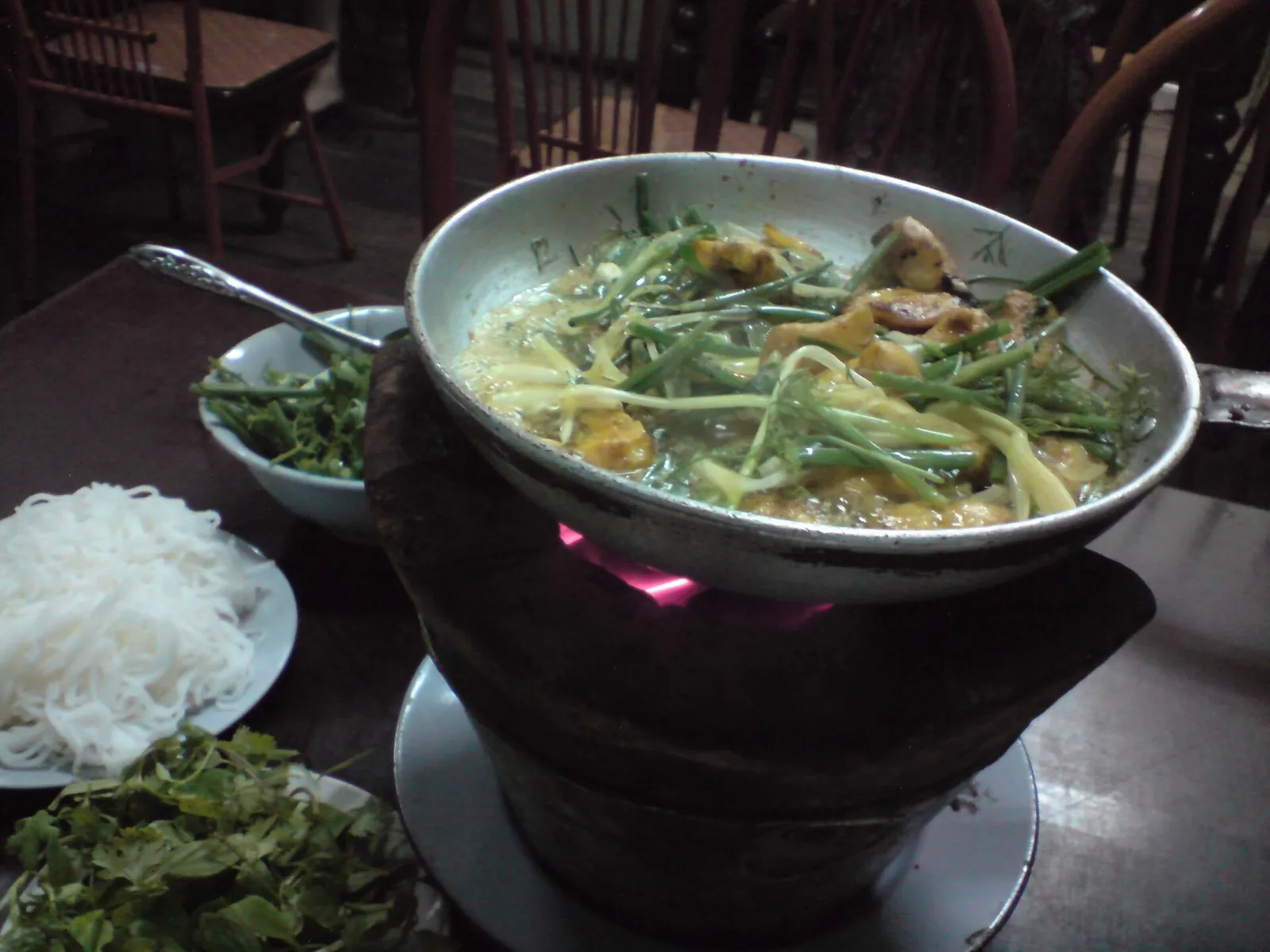 Turmeric fish frying with dill and spring onion in a pan over a table burner, with noodles and herbs beside it