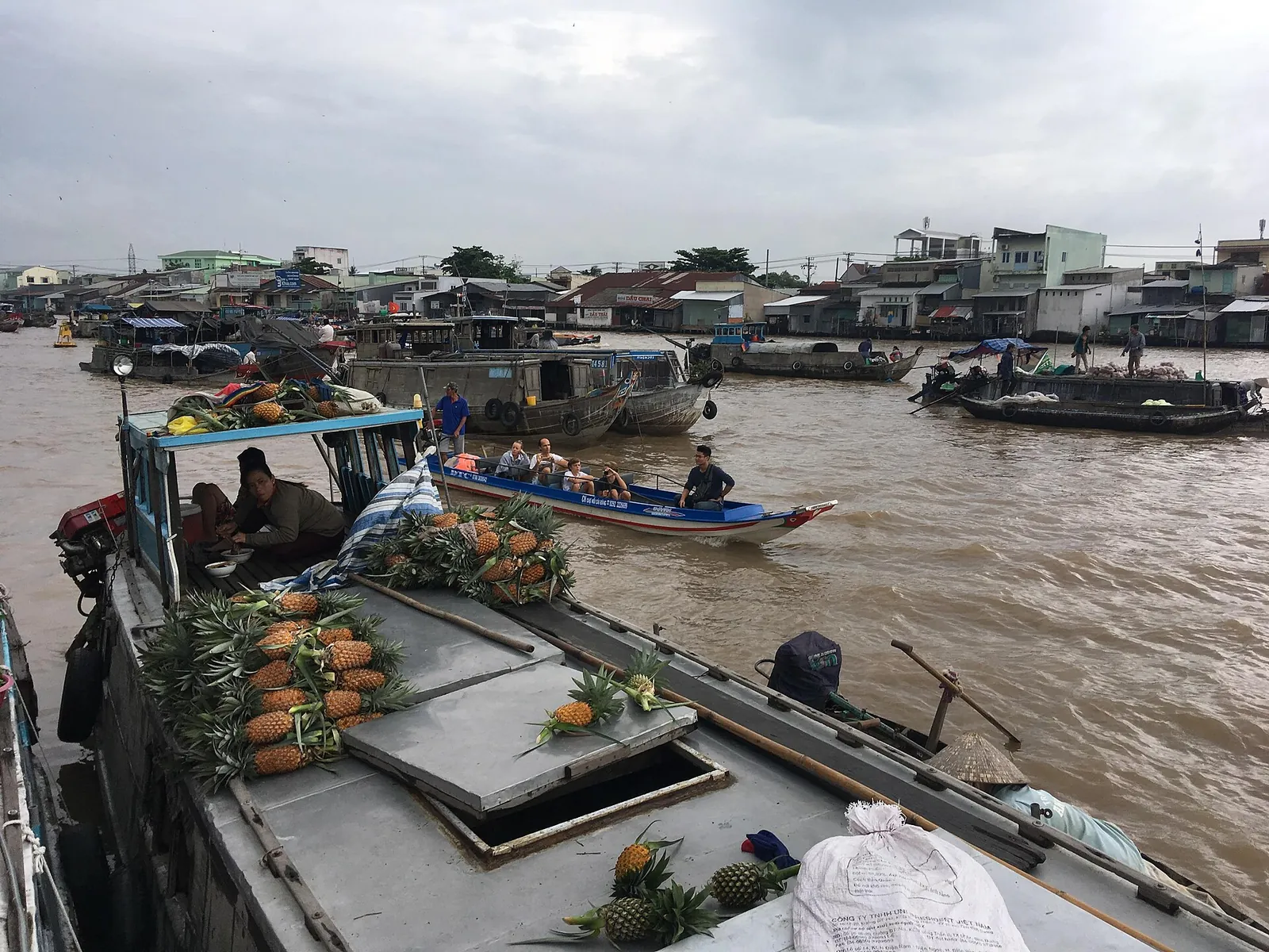 Boat loaded with pineapples among other wooden boats on the brown water of the Cai Rang floating market near Can Tho