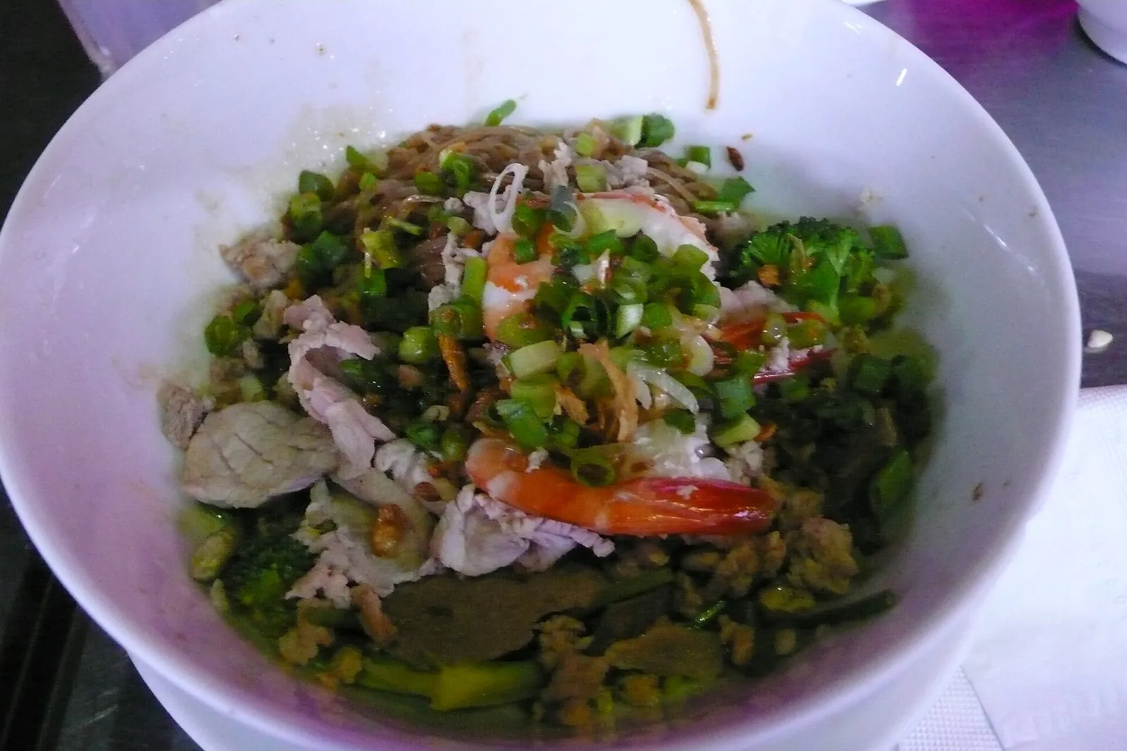 A bowl of dry rice noodles topped with prawns, pork, herbs and fried shallots