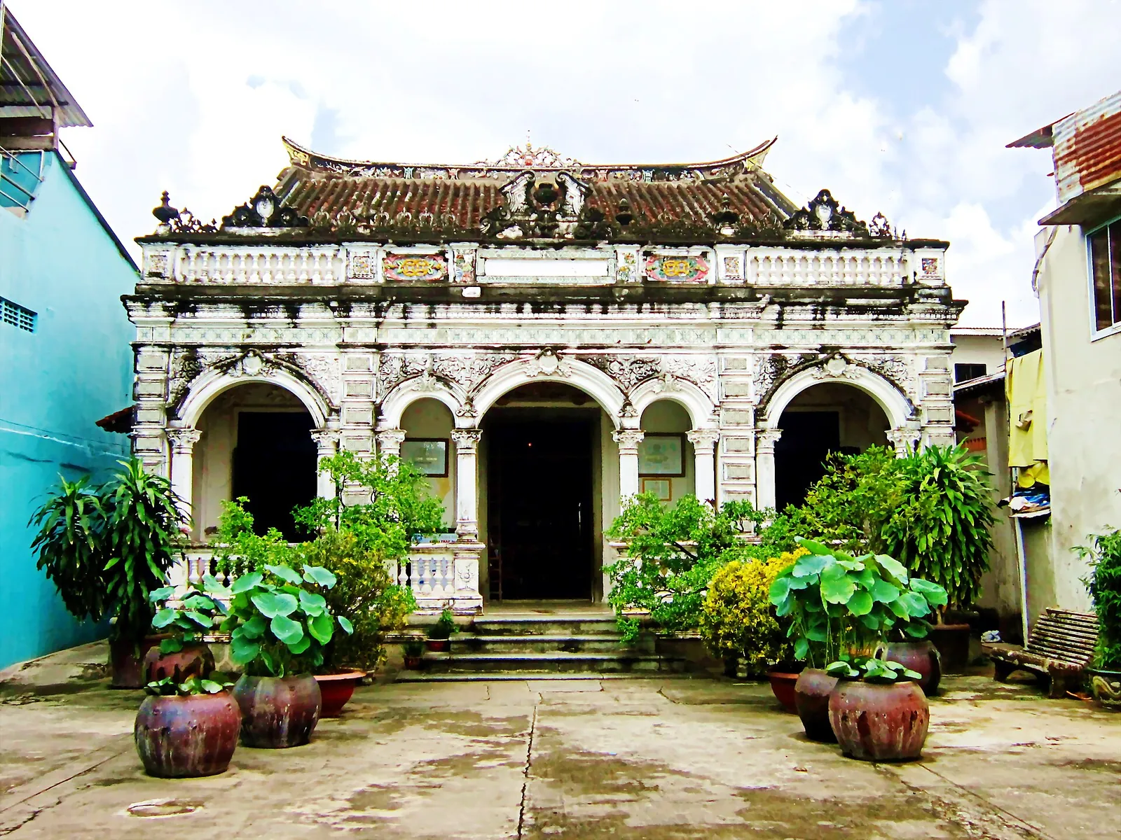 The white arched facade of the Huynh Thuy Le ancient house in Sa Dec, with a curved Chinese-style roof and potted plants in front