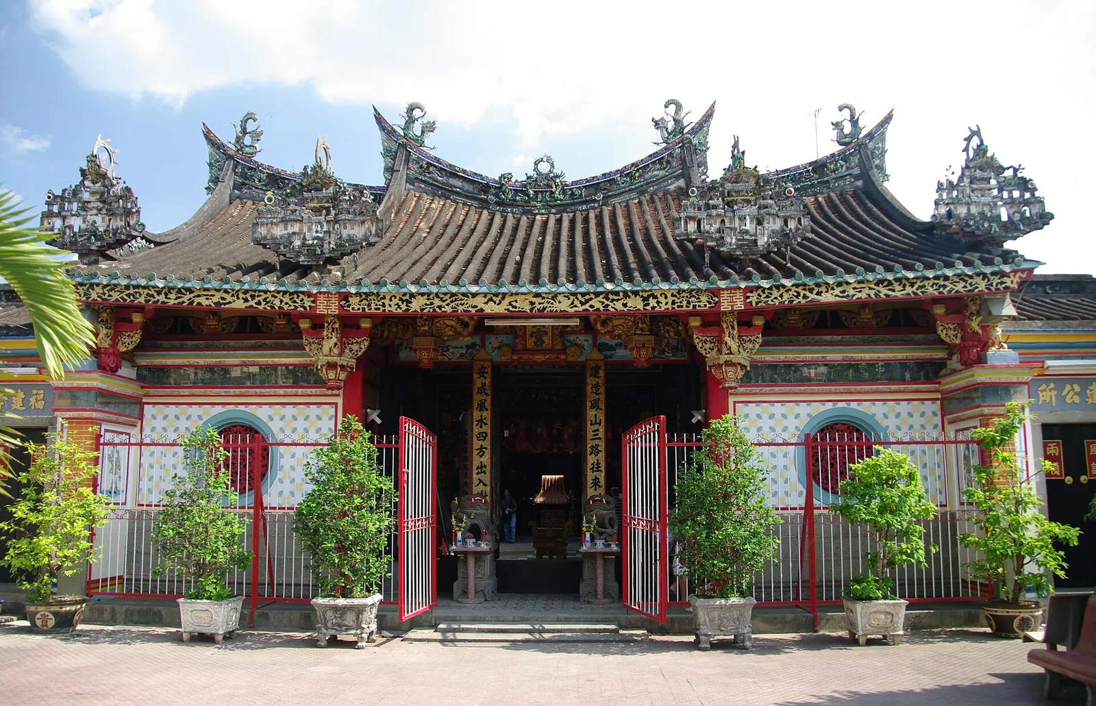 The front of Kien An Cung temple in Sa Dec, with a tiled roof lined with ornate ridge decorations and potted plants by the gates