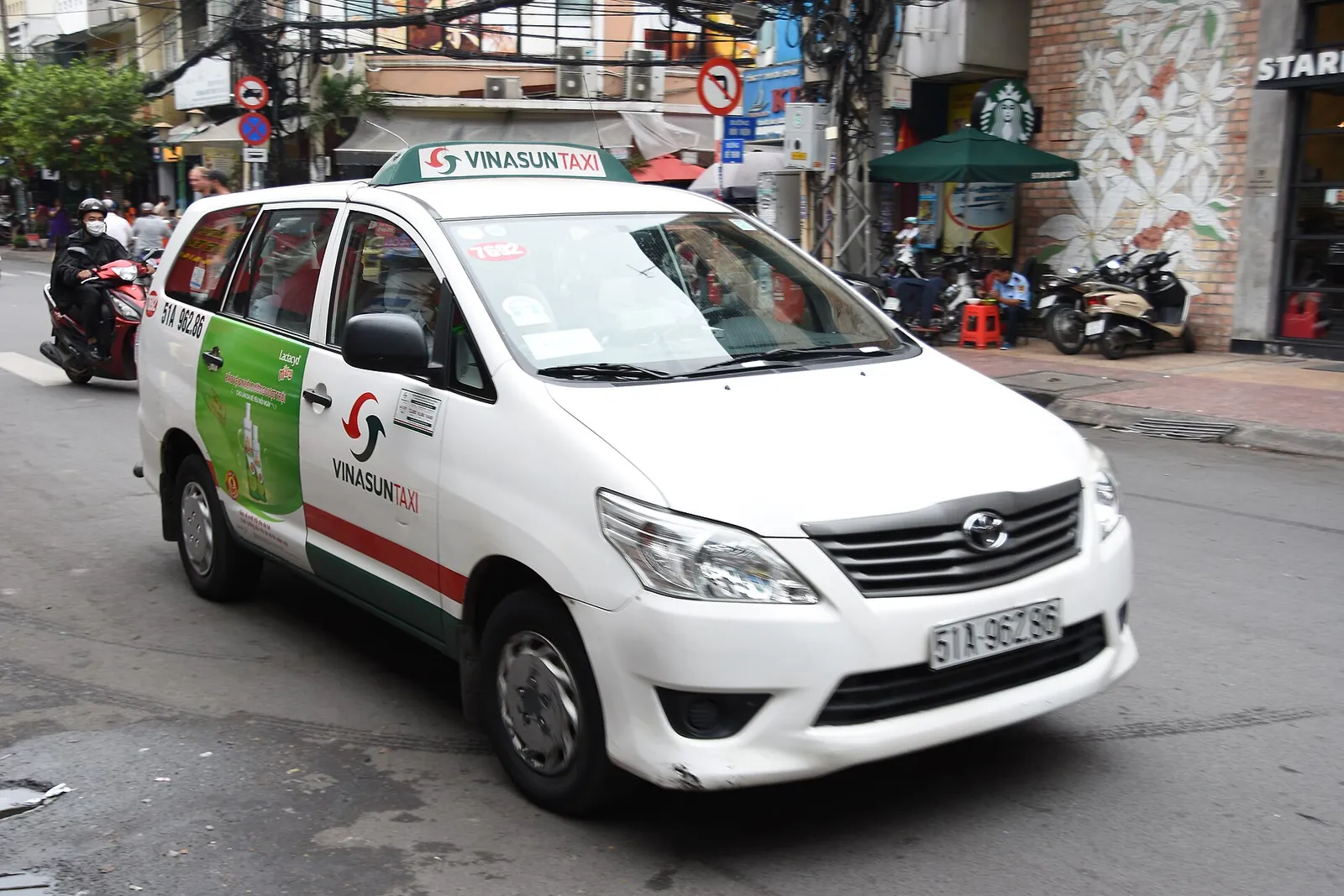 A white Vinasun taxi with green and red stripes parked on a street in Ho Chi Minh City