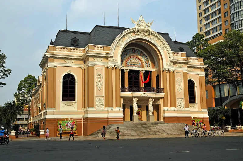 Front of the Saigon Opera House with its arched entrance and steps under a pale sky, high-rise towers behind