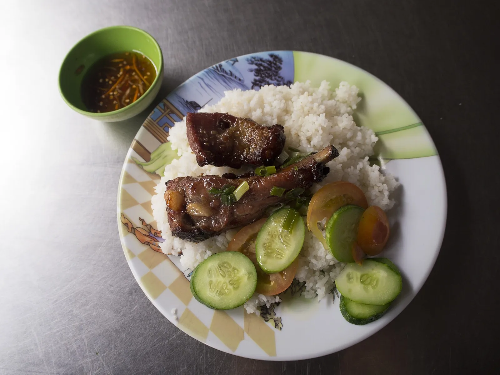 A plate of com tam broken rice with grilled pork, cucumber and a small bowl of fish sauce
