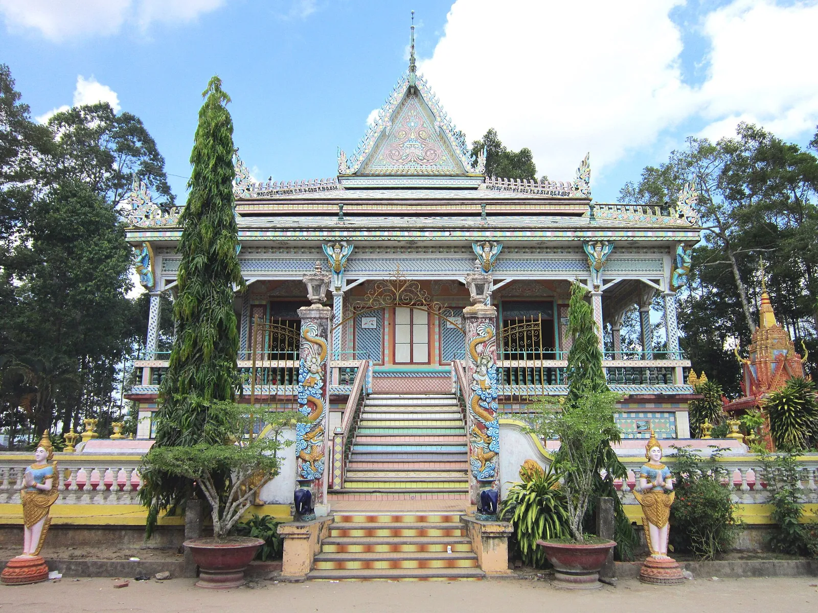 Main hall of Sa Lon Pagoda with ornate pillars, steps and a Khmer-style roof among trees