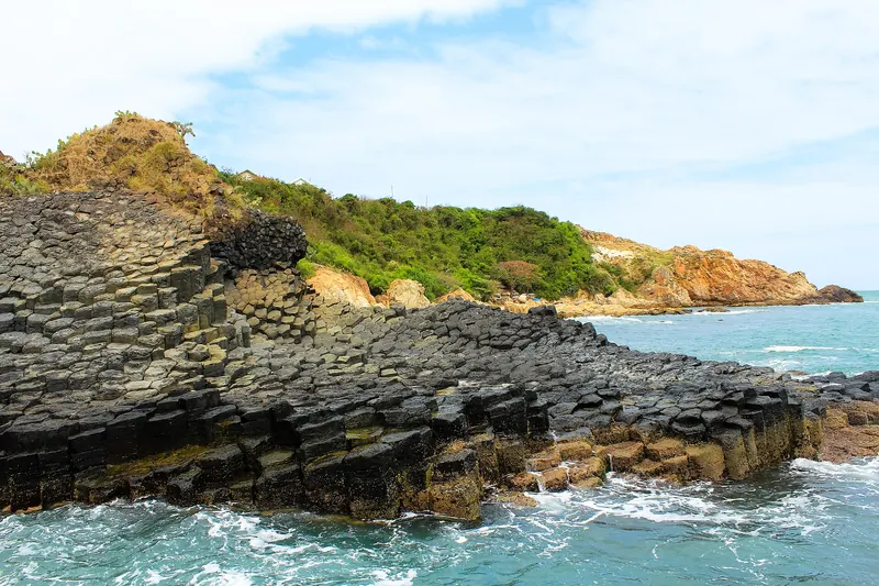 Hexagonal basalt columns of Ganh Da Dia stepping down into the sea below a green headland