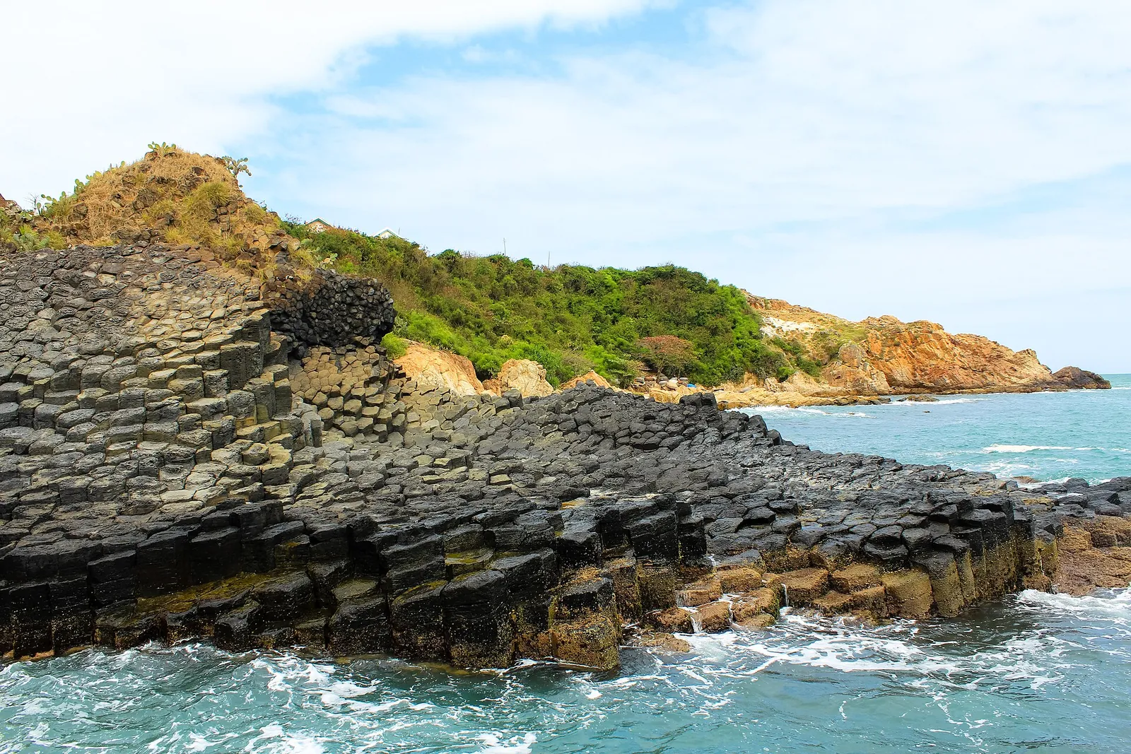 Hexagonal basalt columns of Ganh Da Dia stepping down into the sea below a green headland