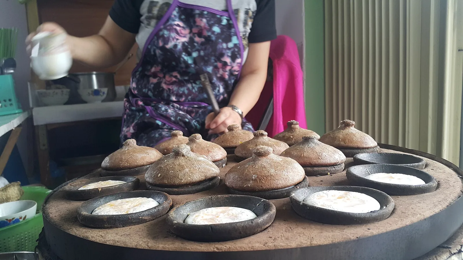 A cook tending rows of small clay moulds of bánh căn rice cakes