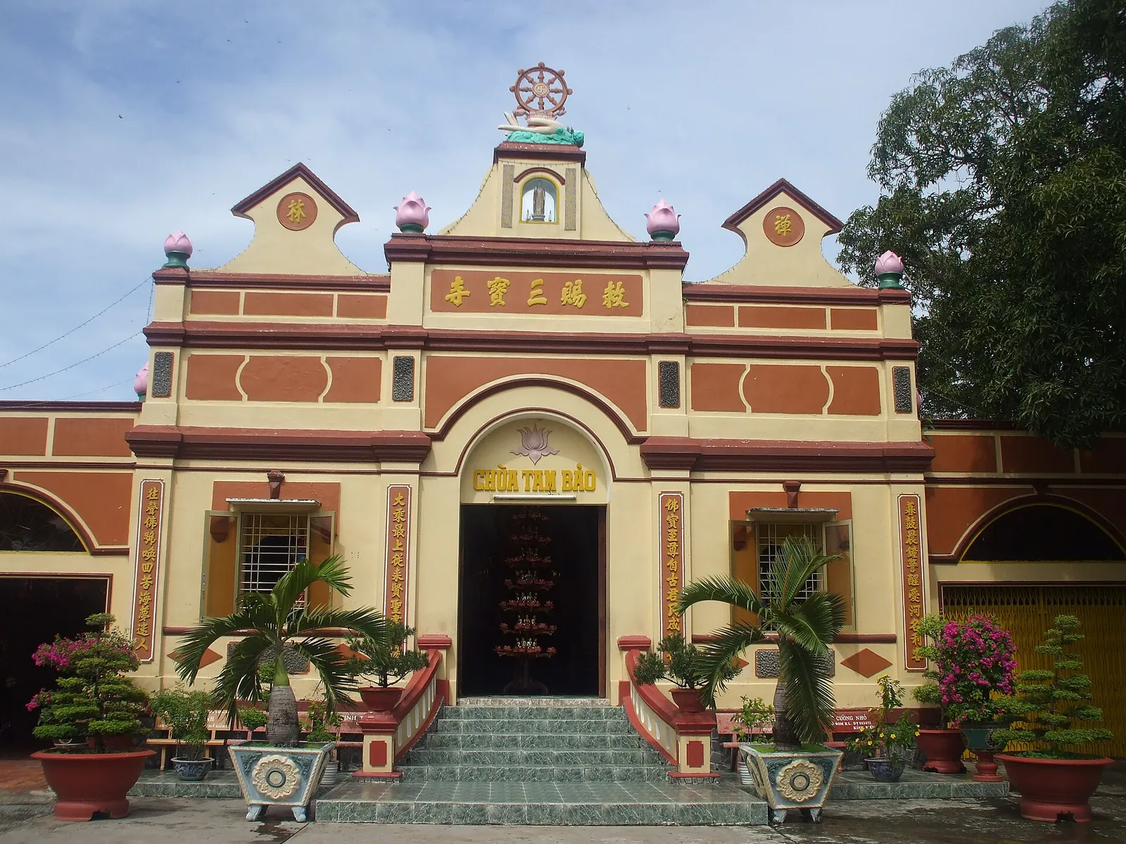 Yellow and red facade of Tam Bao pagoda in Ha Tien with potted plants by the steps